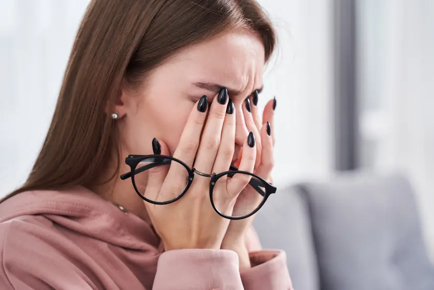 Woman with glasses rubbing her dry and irritated eyes